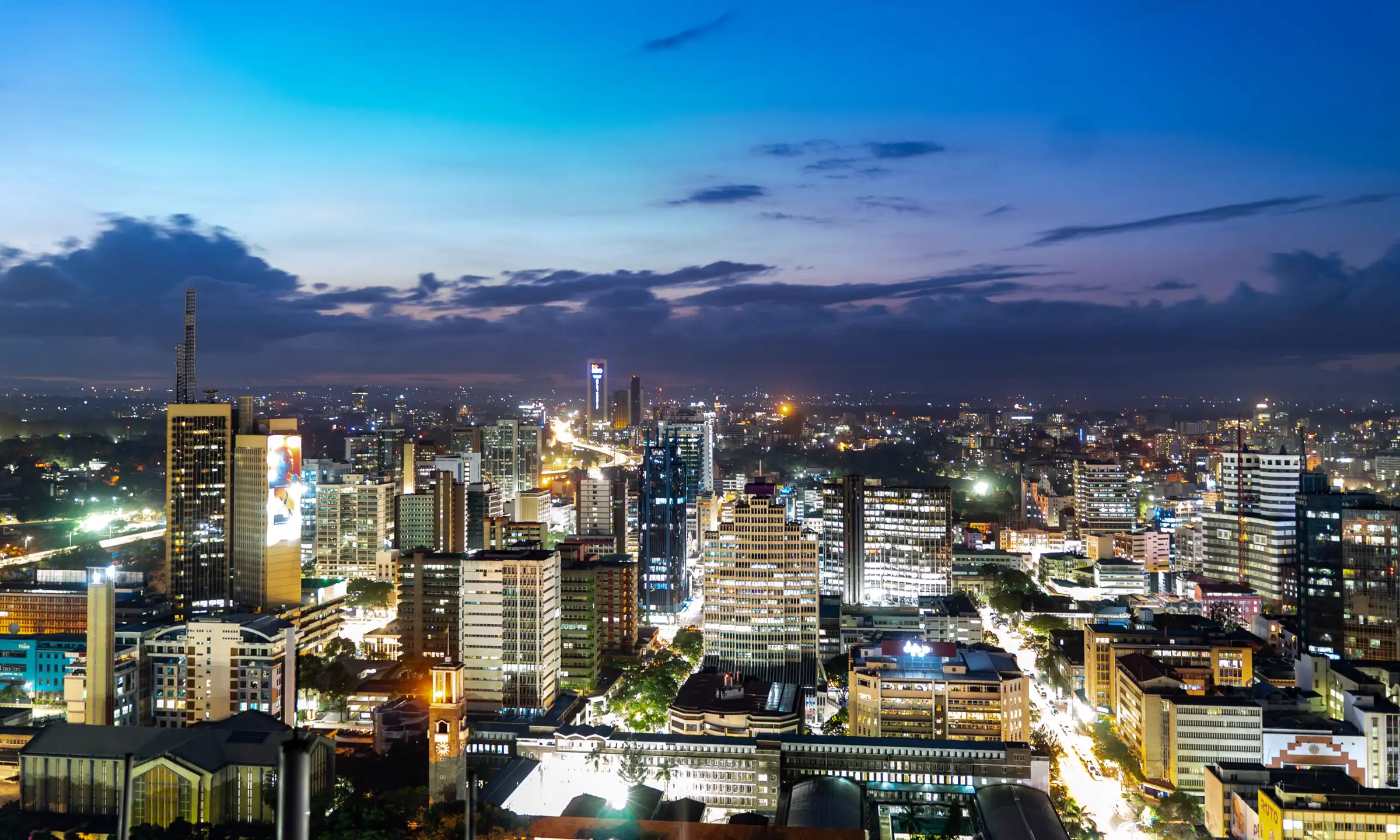 The Nairobi skyline at dusk, with office towers lit against a deep blue sky.